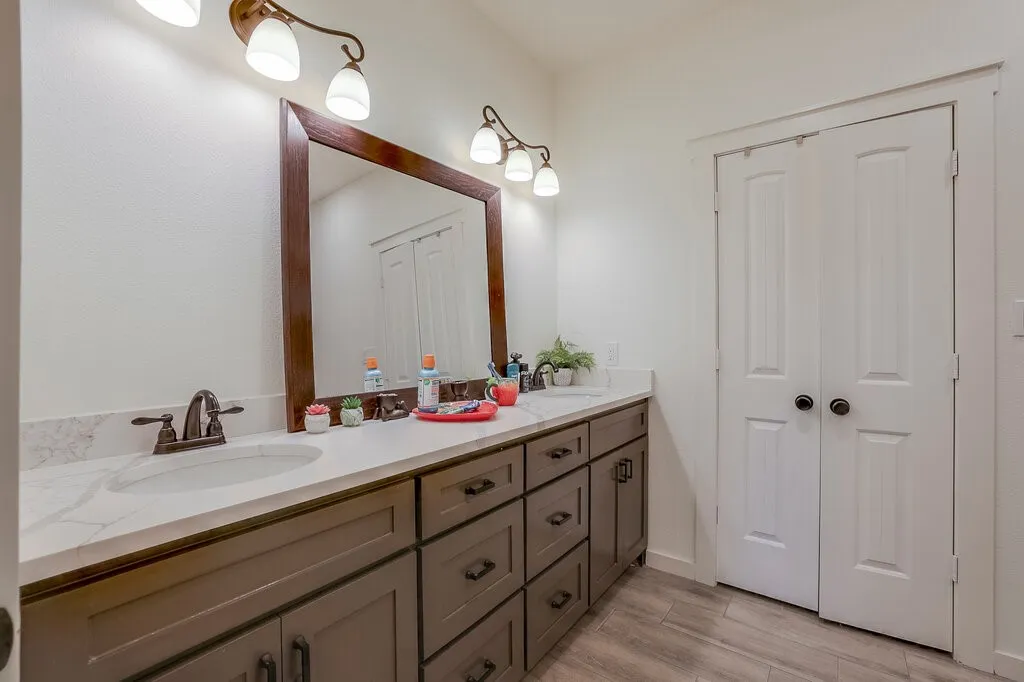 Dual vanities with undermount sinks, bronze-finish hardware, wood-finish cabinetry, and a large framed mirror