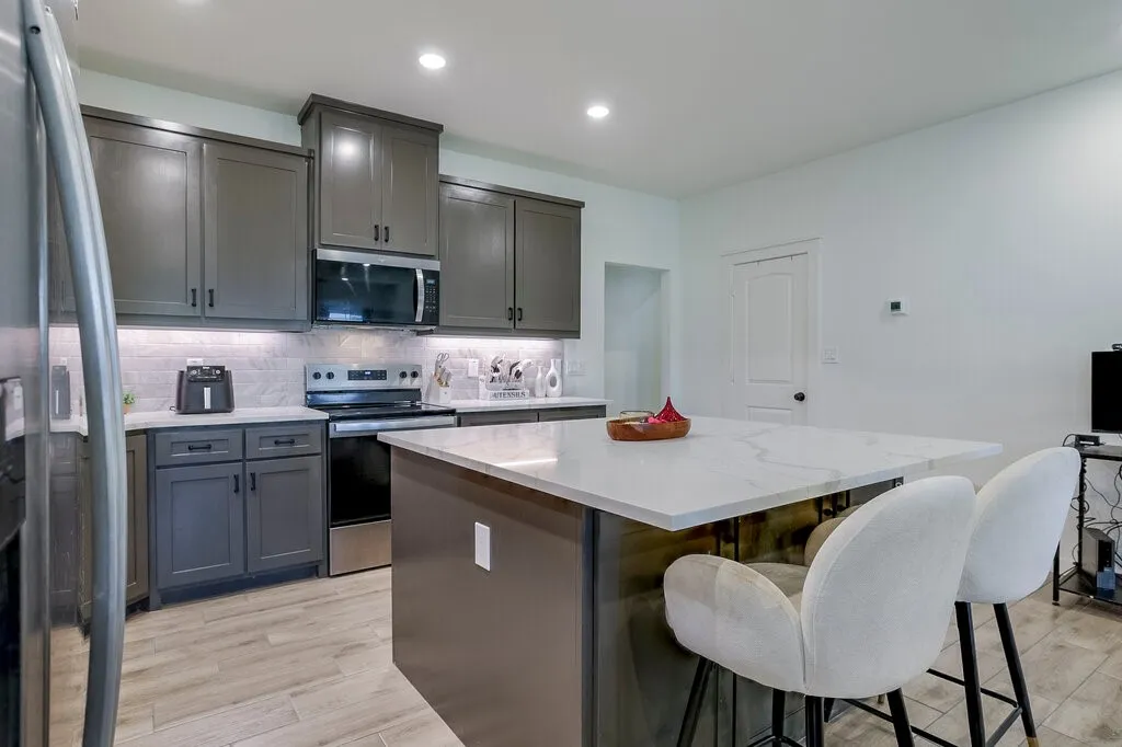 Kitchen featuring a large center island with a light-toned countertop, wood-finish flooring, dark gray cabinetry, stainless steel appliances, and recessed lighting
