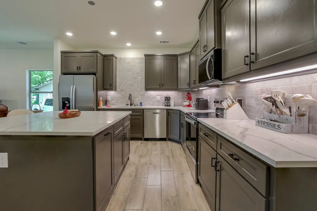 Spacious kitchen featuring an expansive island, gray cabinetry, light-toned countertops, and wood-finish flooring