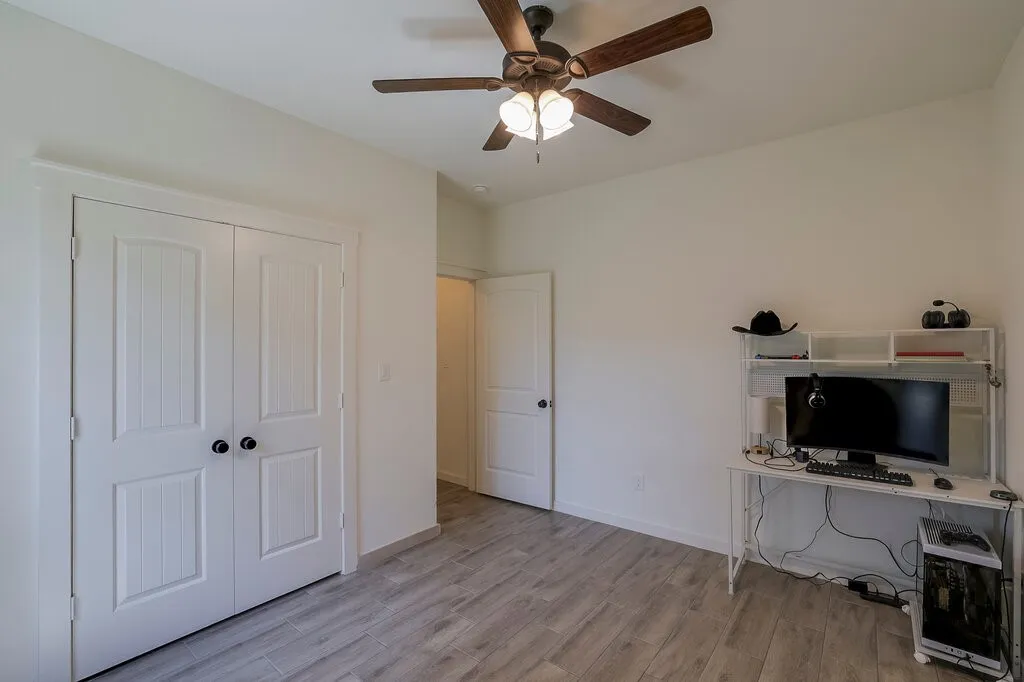 Ceiling fan with light fixture, wood-finish flooring, white paneled double doors with black hardware, and white interior walls