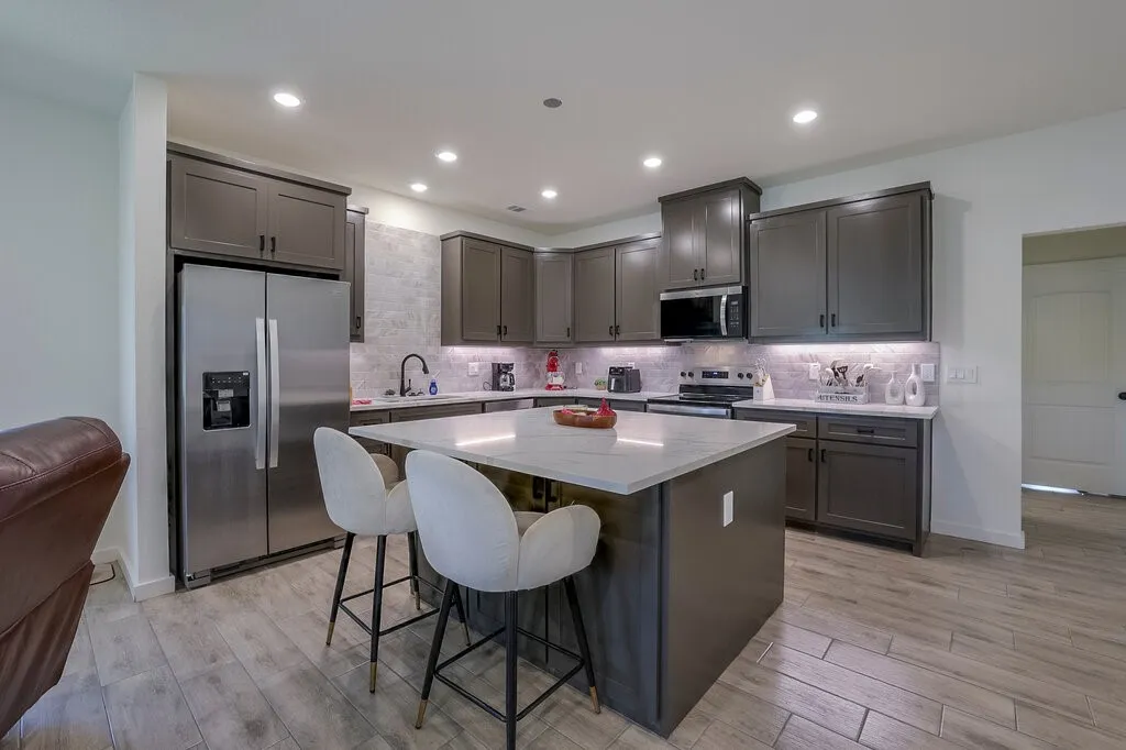 Modern kitchen featuring stainless steel appliances, dark wood-finish cabinetry, a large center island with a light-toned countertop, and wood-finish tile flooring