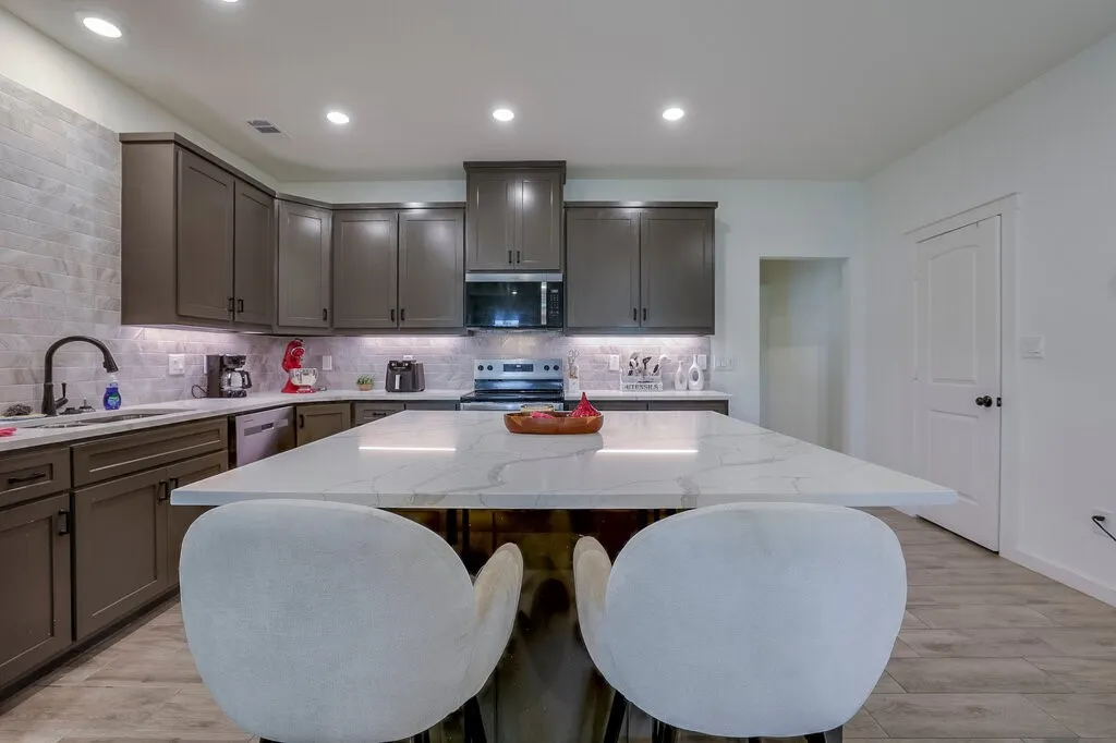 Expansive kitchen island with a light-toned countertop, ample dark-toned cabinetry, recessed lighting, and wood-finish flooring
