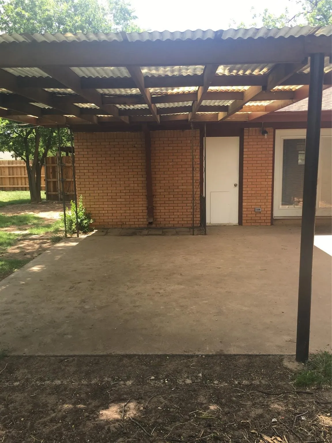 Patio with a corrugated roof covering, brick wall, and a wood fence in the​​‌​​​​‌​​‌‌​‌‌​​​‌‌​‌​‌​‌​​​‌​​ background