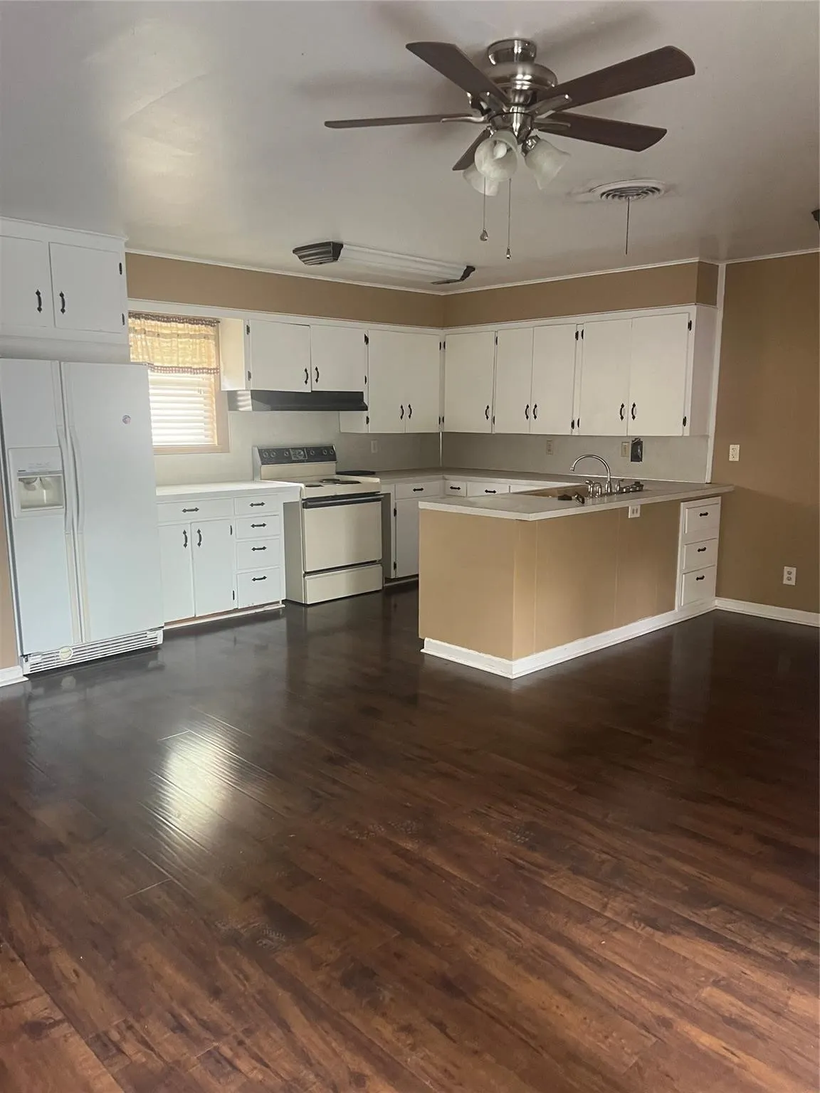 Kitchen featuring wood-finish flooring, white cabinetry, a kitchen island with a built-in sink, and a ceiling fan
