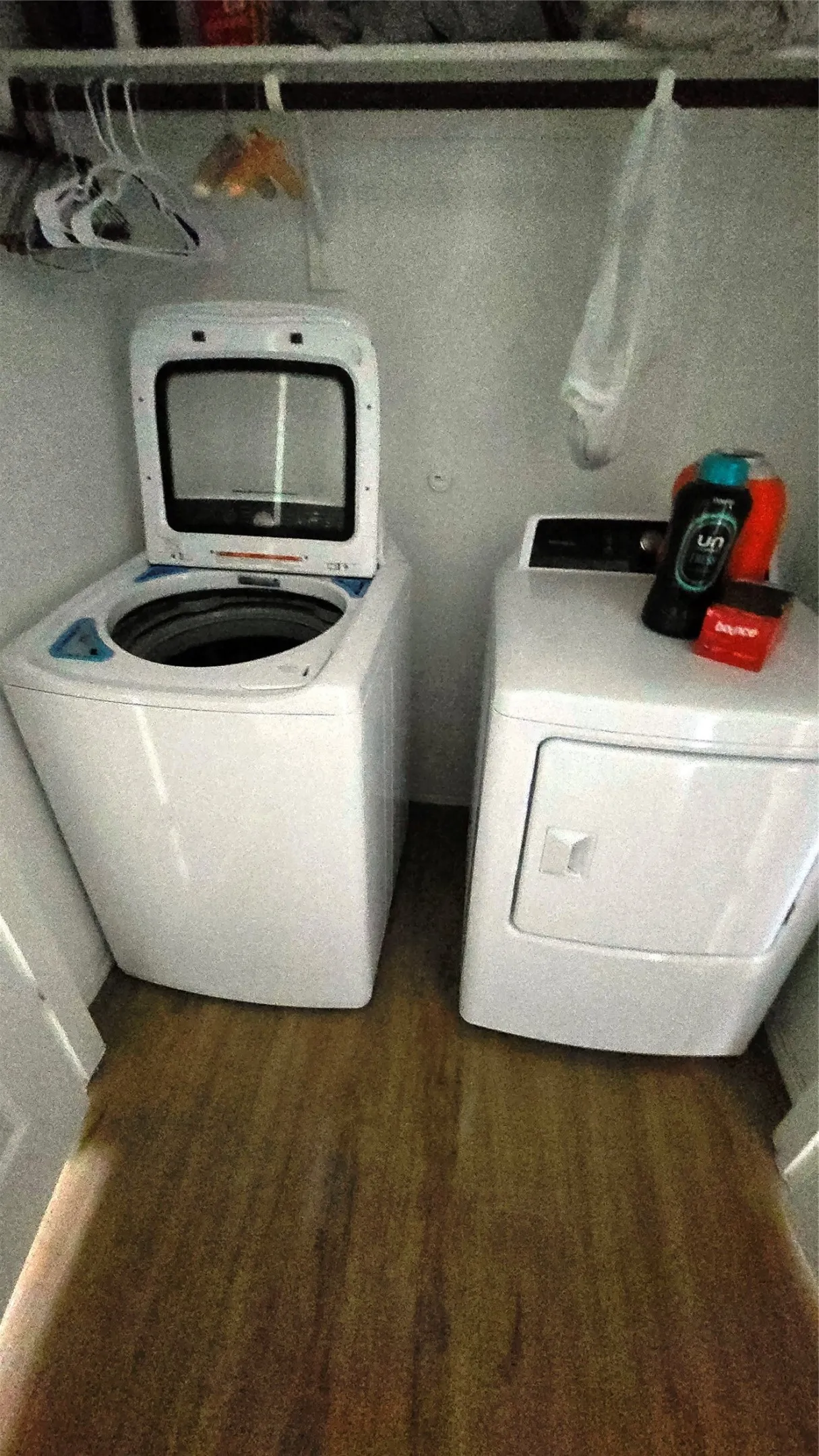 Dedicated laundry area featuring a white top-load washing machine, a white front-load dryer, wood-finish flooring, and an upper storage shelf