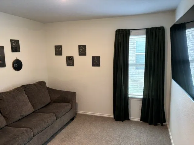 Comfortable 4th bedroom used as a media room featuring neutral wall finishes, carpet flooring, and large windows dressed with black drapery