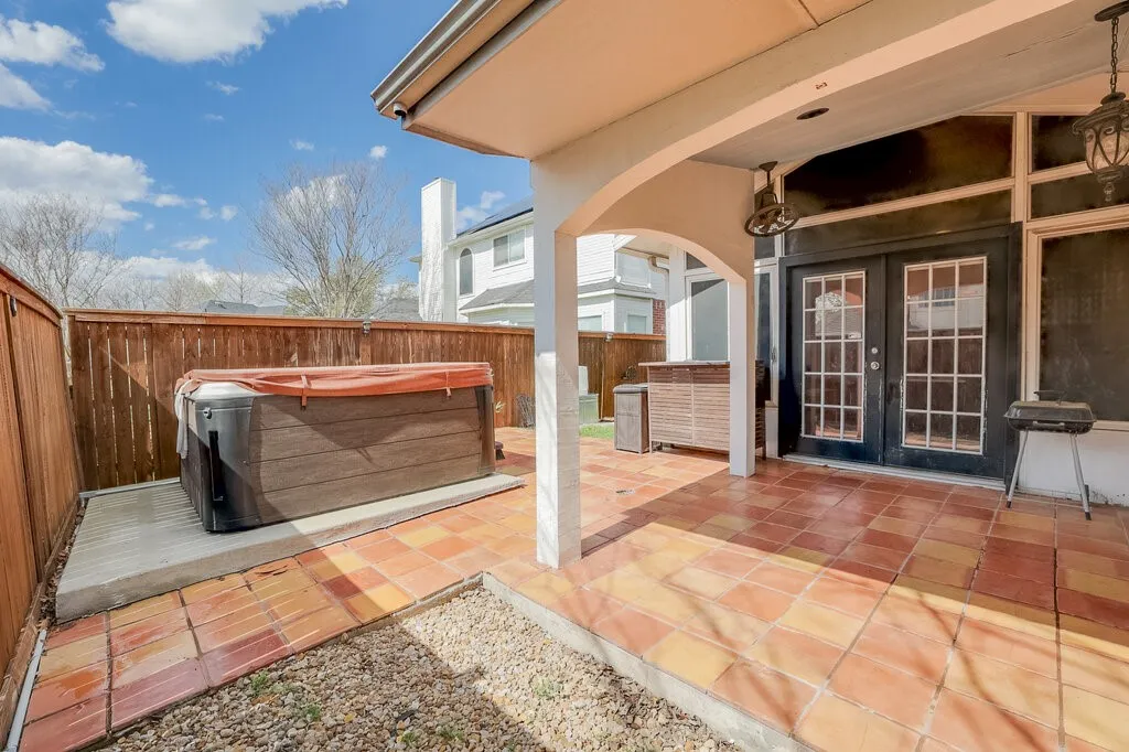 Covered patio featuring terra cotta tile, integrated hot tub, and wood panel fencing