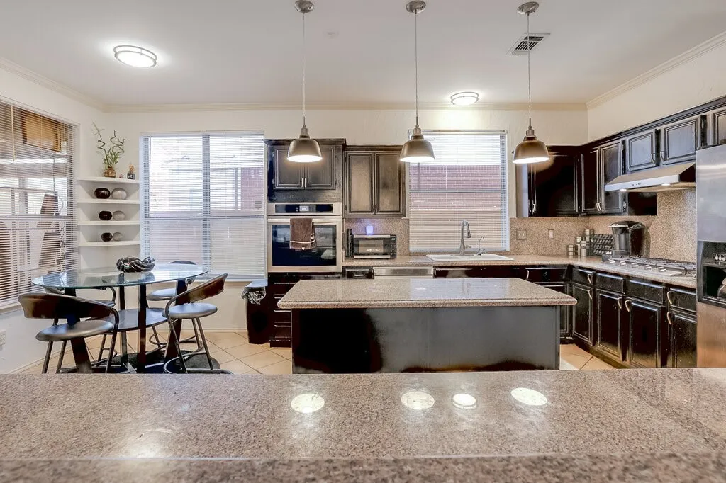 Kitchen featuring dark wood-finish cabinetry, built-in stainless steel appliances, a center island with a granite-style countertop, and recessed lighting