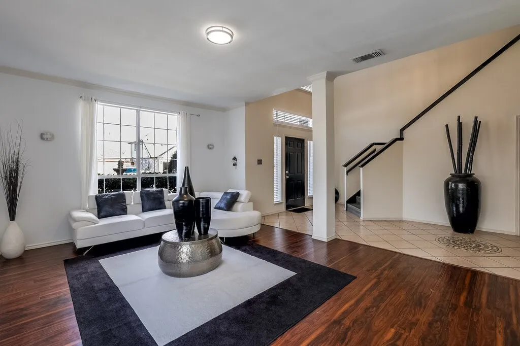 Hardwood-finish flooring, large multi-pane windows, recessed ceiling lighting, staircase with dark railing, and tile flooring with decorative inlay