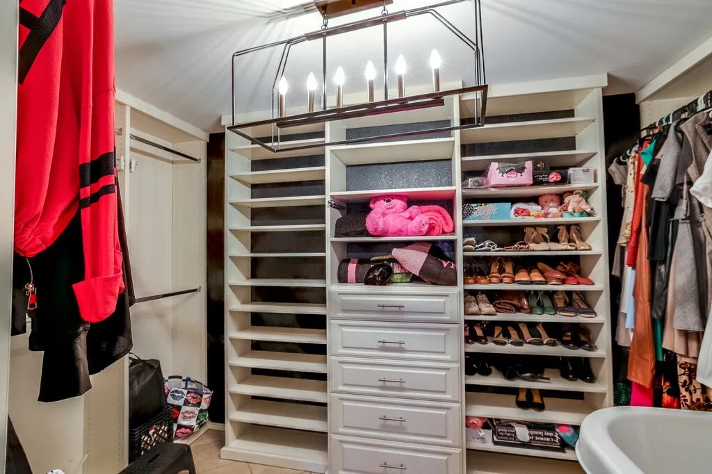 Custom walk-in closet featuring extensive built-in shelving with adjustable shelves, integrated storage drawers, a modern linear pendant light fixture, and organized display space for accessories and footwear