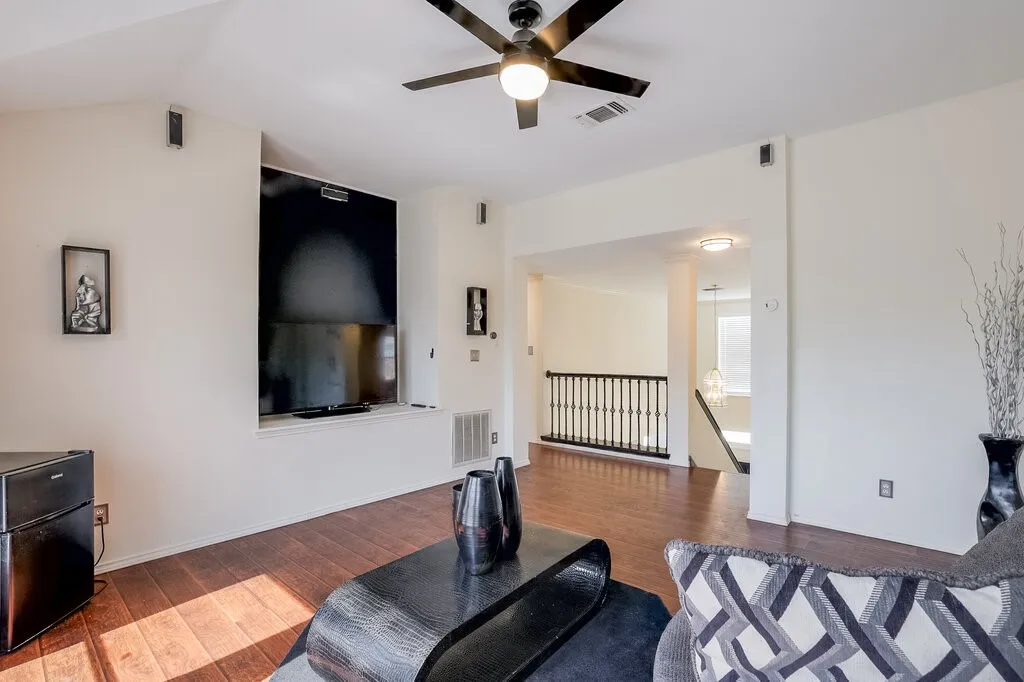 Vaulted ceiling with a ceiling fan, wood-finish flooring, built-in media niche, and wrought iron staircase railing