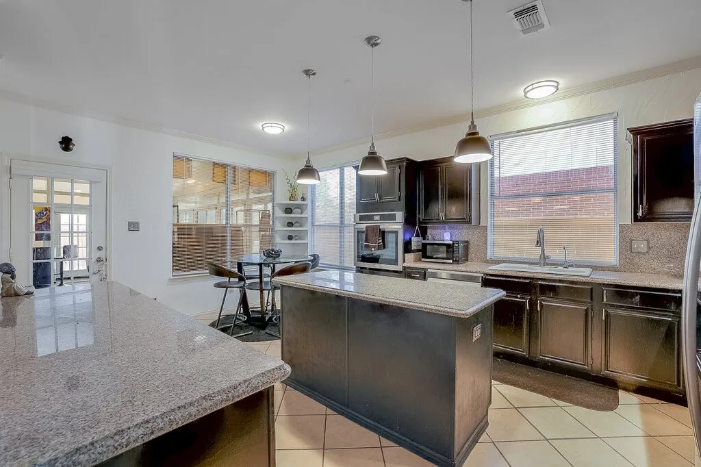 Kitchen featuring dark wood cabinetry, light-toned countertops, a central island, stainless steel appliances, and tiled flooring