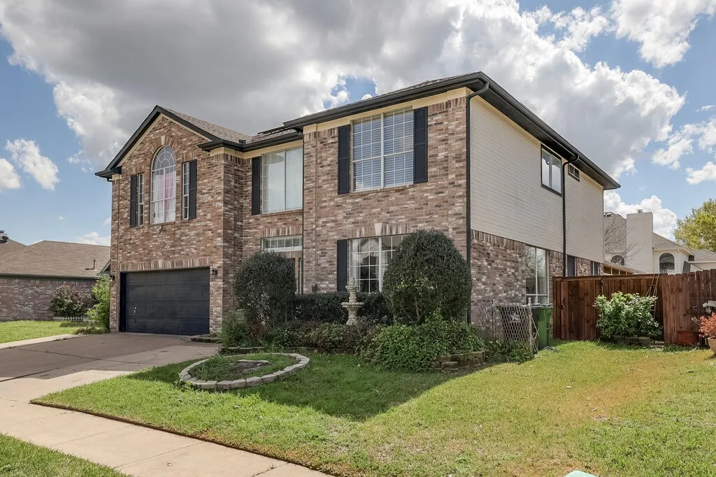Brick exterior with siding accents, attached garage, arched window, and mature landscaping