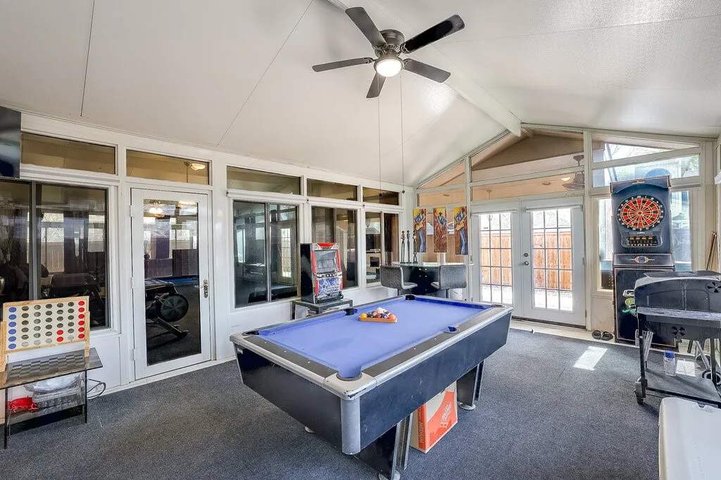 Enclosed sunroom featuring a vaulted ceiling with a ceiling fan, multiple windows, and exterior access via double doors