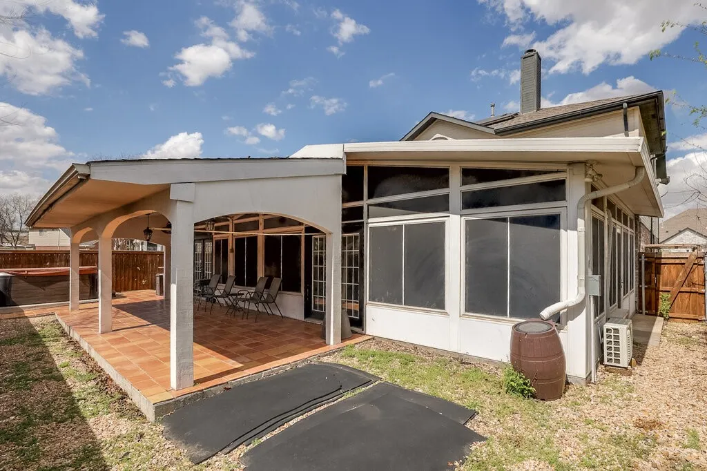 Expansive covered patio with tiled flooring, enclosed sunroom, exterior hot tub, and wood fencing