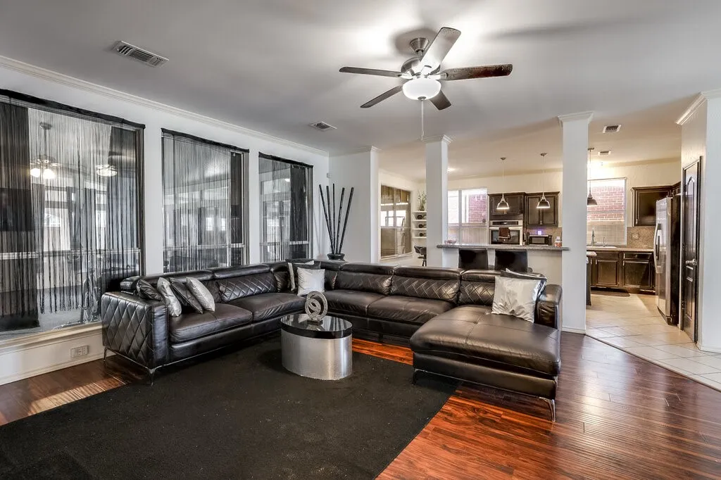 Open-concept living space featuring wood-finish flooring, a ceiling fan with integrated lighting, and multiple large windows