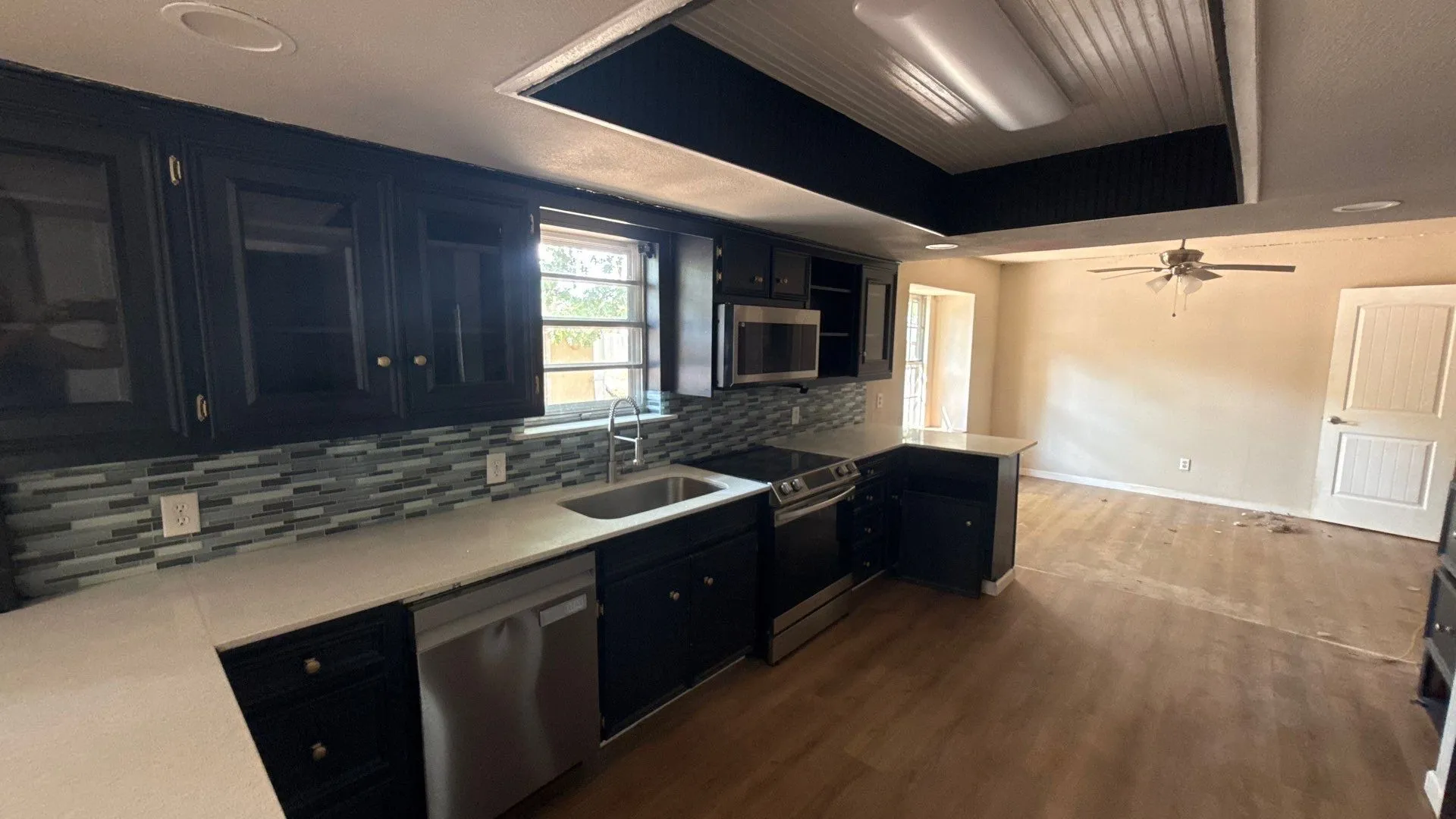 Black cabinetry with stainless steel hardware, white countertops, stainless steel appliances, and a mosaic tile backsplash