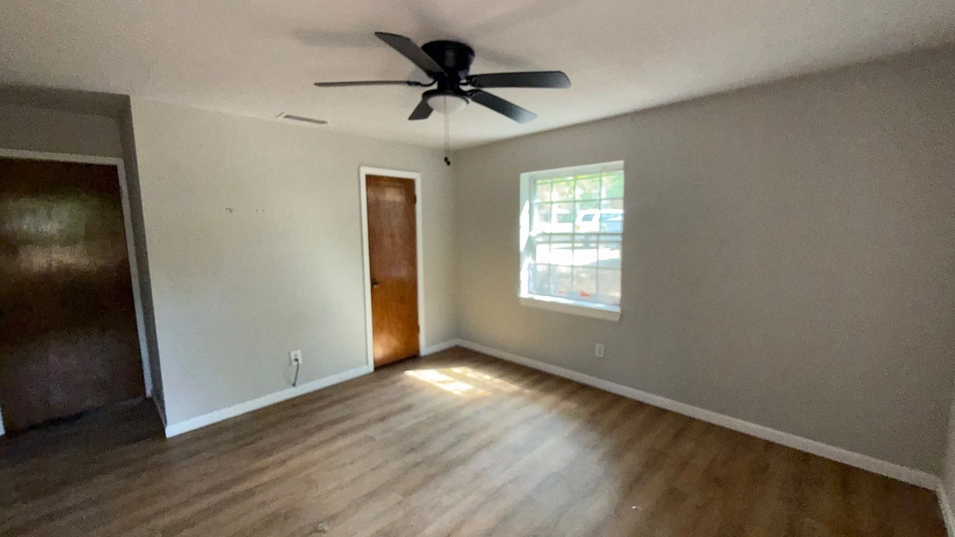 Wood-finish flooring with a ceiling fan, light gray painted walls, and a white-framed window