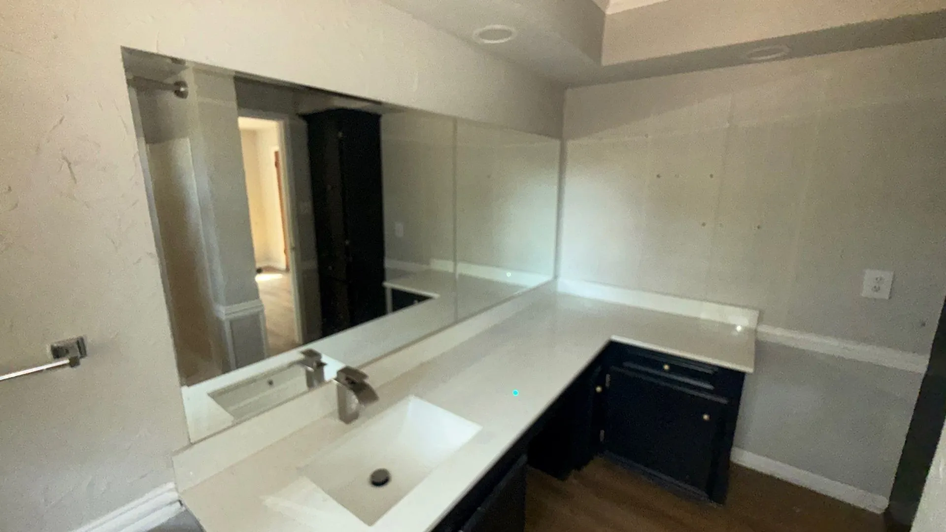 Elongated vanity mirror, single basin sink, brushed nickel faucet, light-toned countertop, and dark wood-finish cabinetry