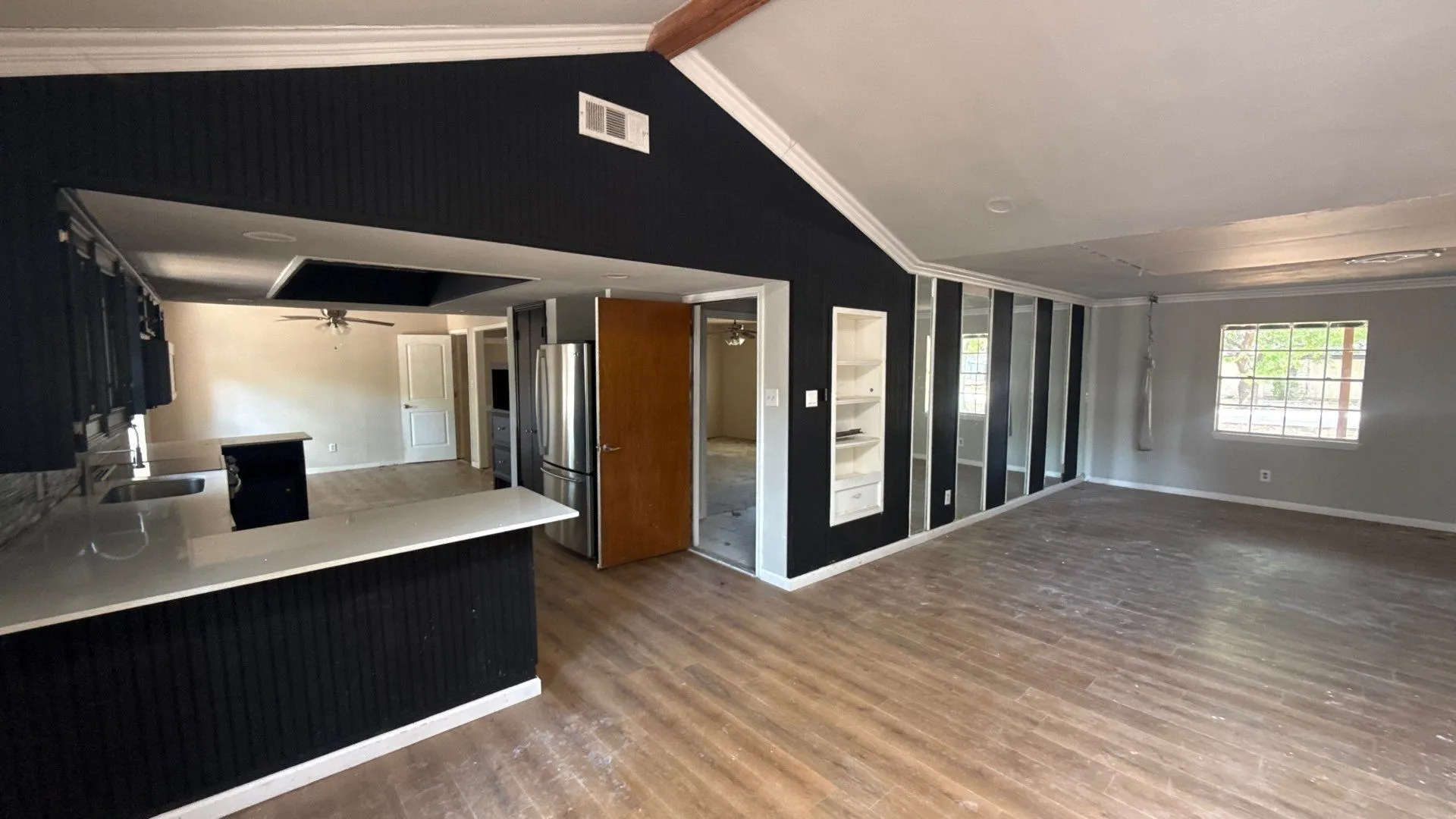 Wood-finish flooring throughout, vaulted ceiling, built-in shelving, and a kitchen island with a light-toned countertop