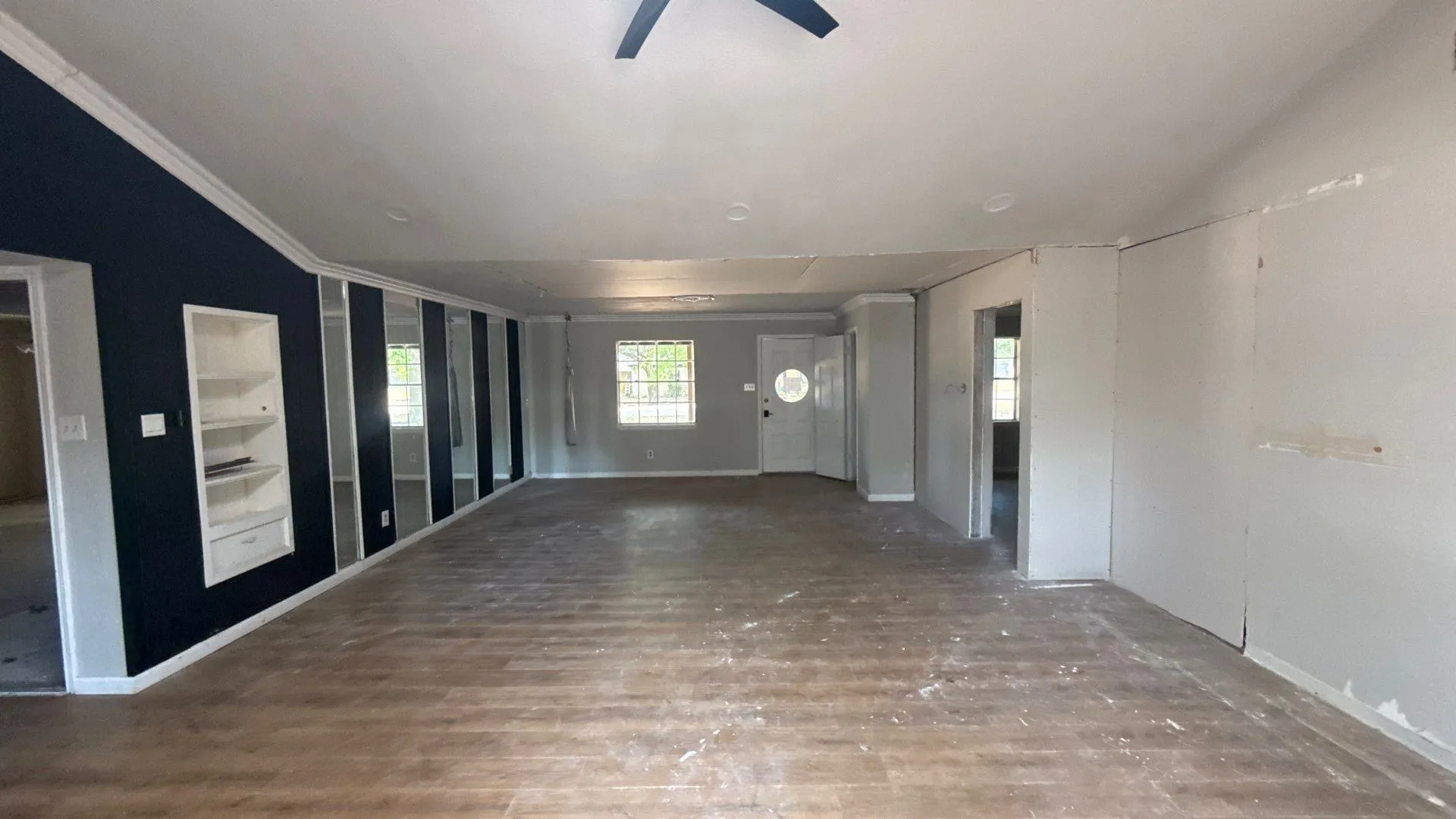 Wood-finish flooring throughout, featuring a dark accent wall with built-in shelving, multiple windows, and a ceiling fan