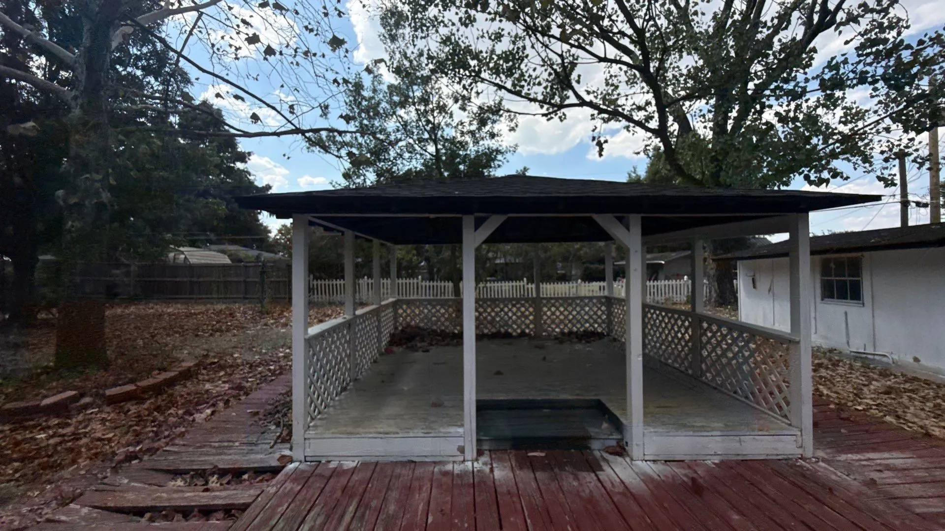 Covered gazebo with lattice railing and a dark shingle roof, complemented by a red-stained wood deck