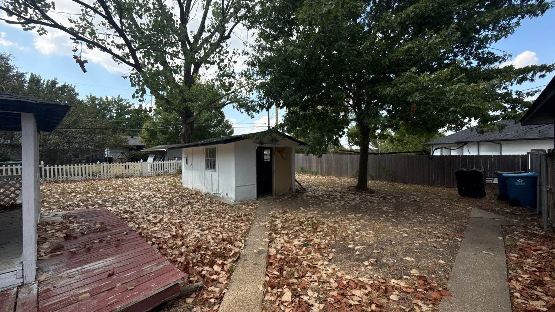 Expansive backyard featuring a mature tree, wooden privacy fence, a storage shed, and a concrete pathway