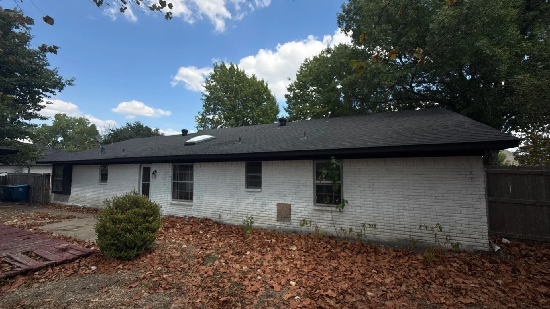 White brick exterior with a dark shingle roof and a skylight