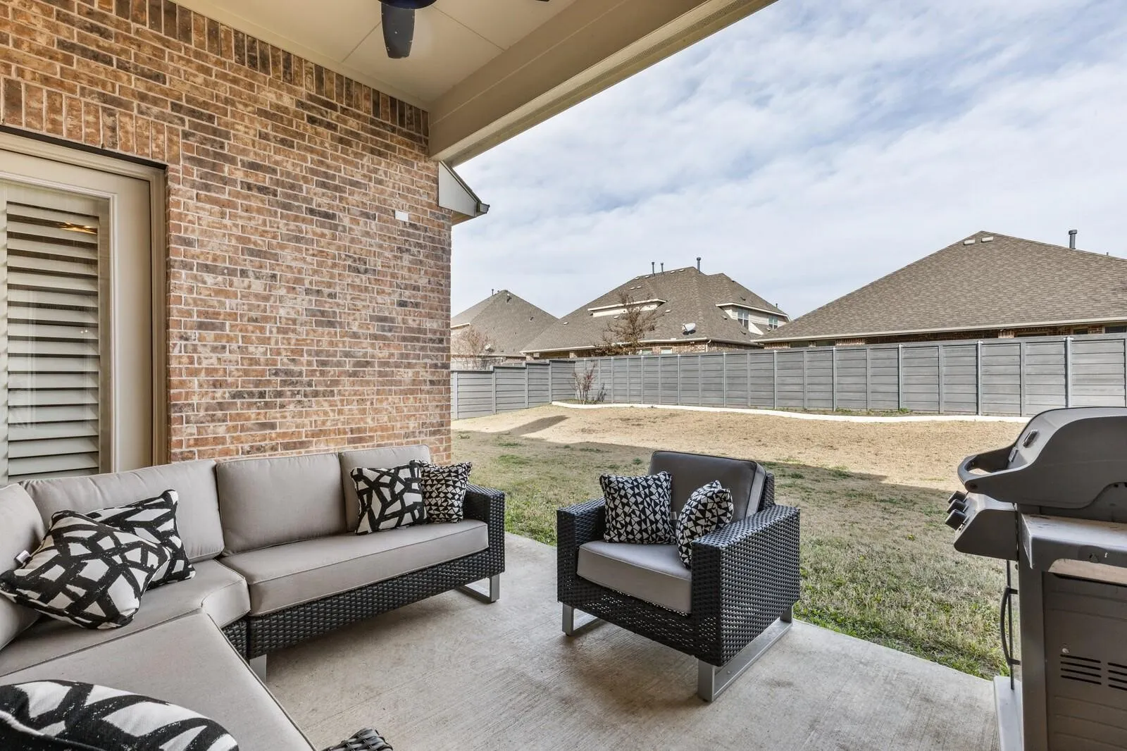 Covered concrete patio with brick wall exterior, ceiling fan, and access to a fenced backyard
