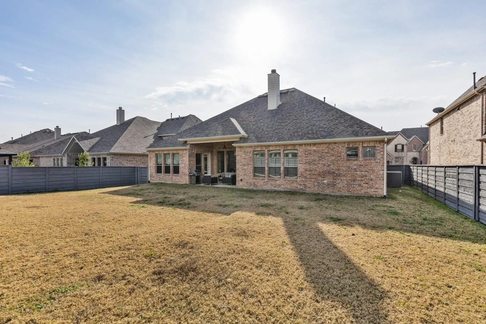 Expansive backyard with a covered patio, brick exterior, and a privacy fence