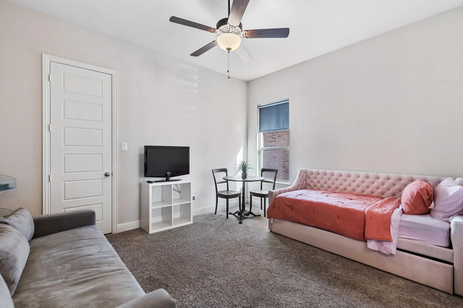 Bright, carpeted bedroom featuring a ceiling fan with integrated lighting, white six-panel closet door, and large window with natural light