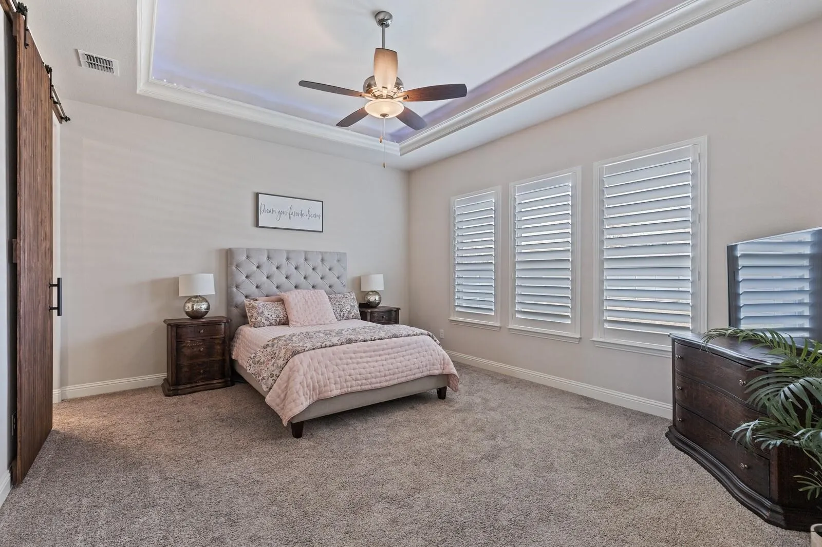 Spacious primary bedroom featuring a tufted upholstered headboard, dual nightstands with table lamps, and neutral wall finishes