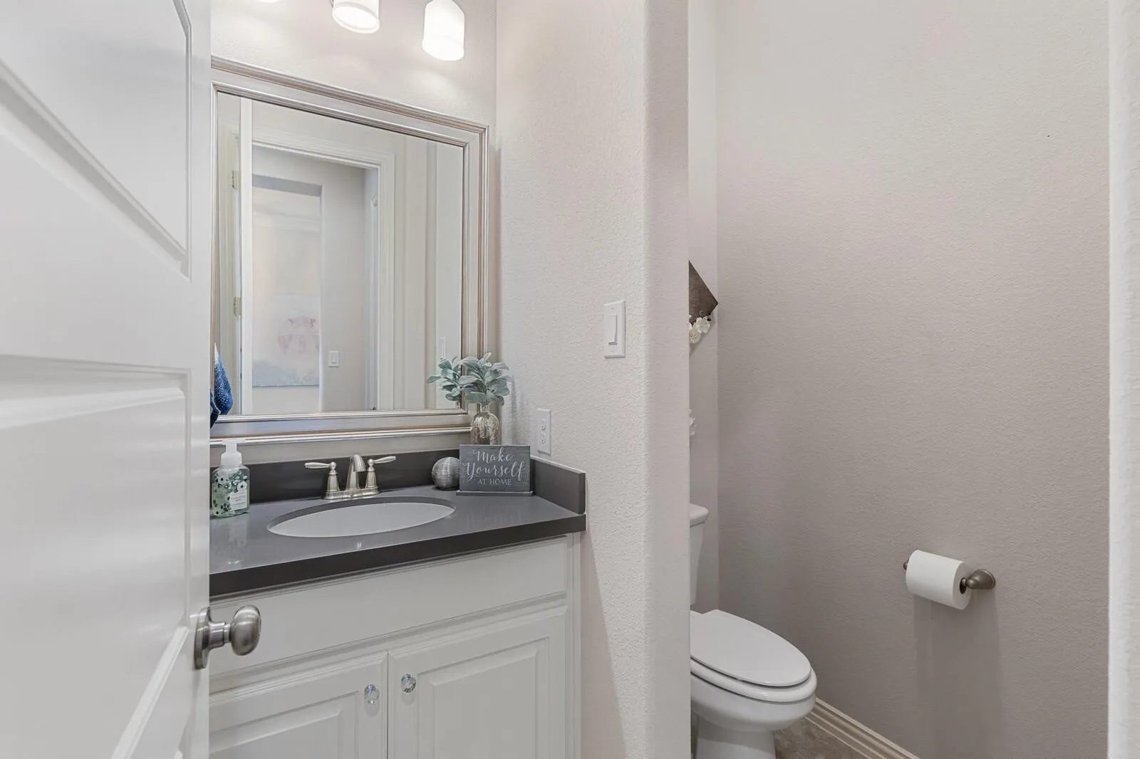 Modern half bath featuring a white vanity with dark countertop, chrome faucet, and large framed mirror