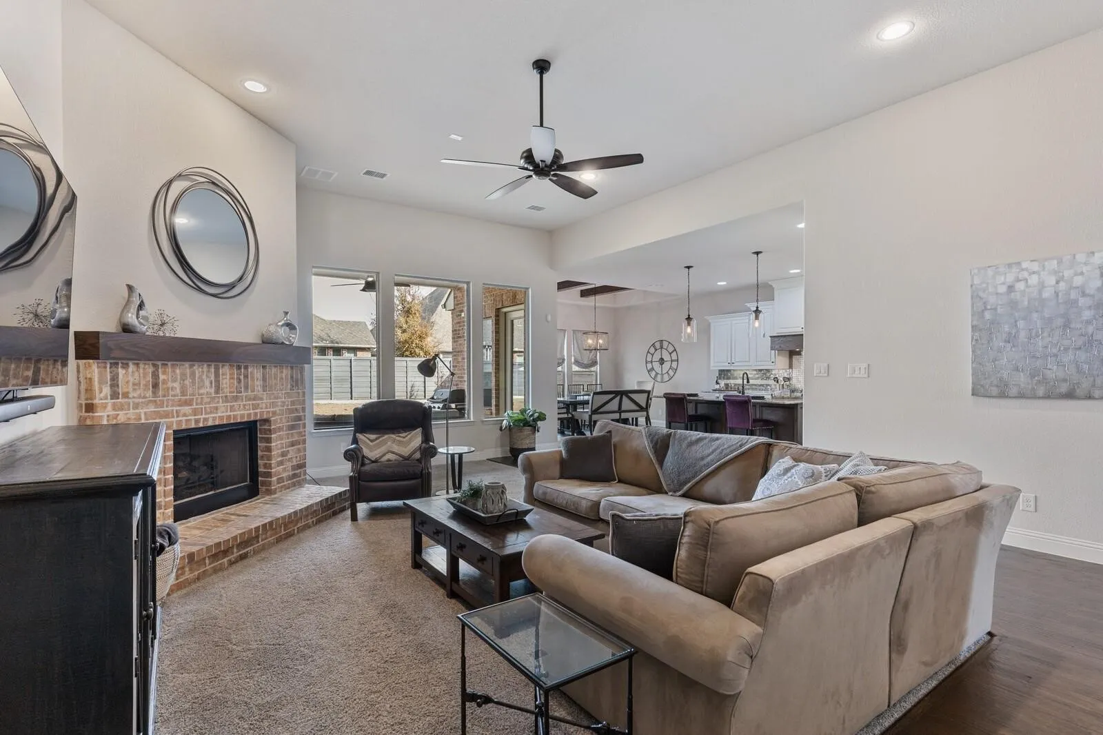 Open-concept living area featuring a two-way gas fireplace with brick surround, hardwood flooring throughout, recessed lighting, and a ceiling fan