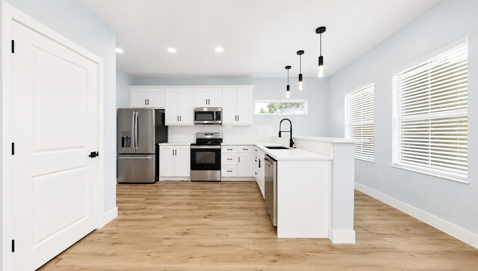 Open-concept kitchen with white cabinetry, stainless steel appliances, wood-finish flooring, and recessed lighting