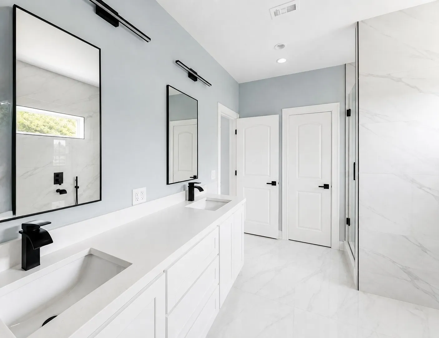 Dual vanity with matte black fixtures, quartz countertops, white cabinetry, and large format tile flooring