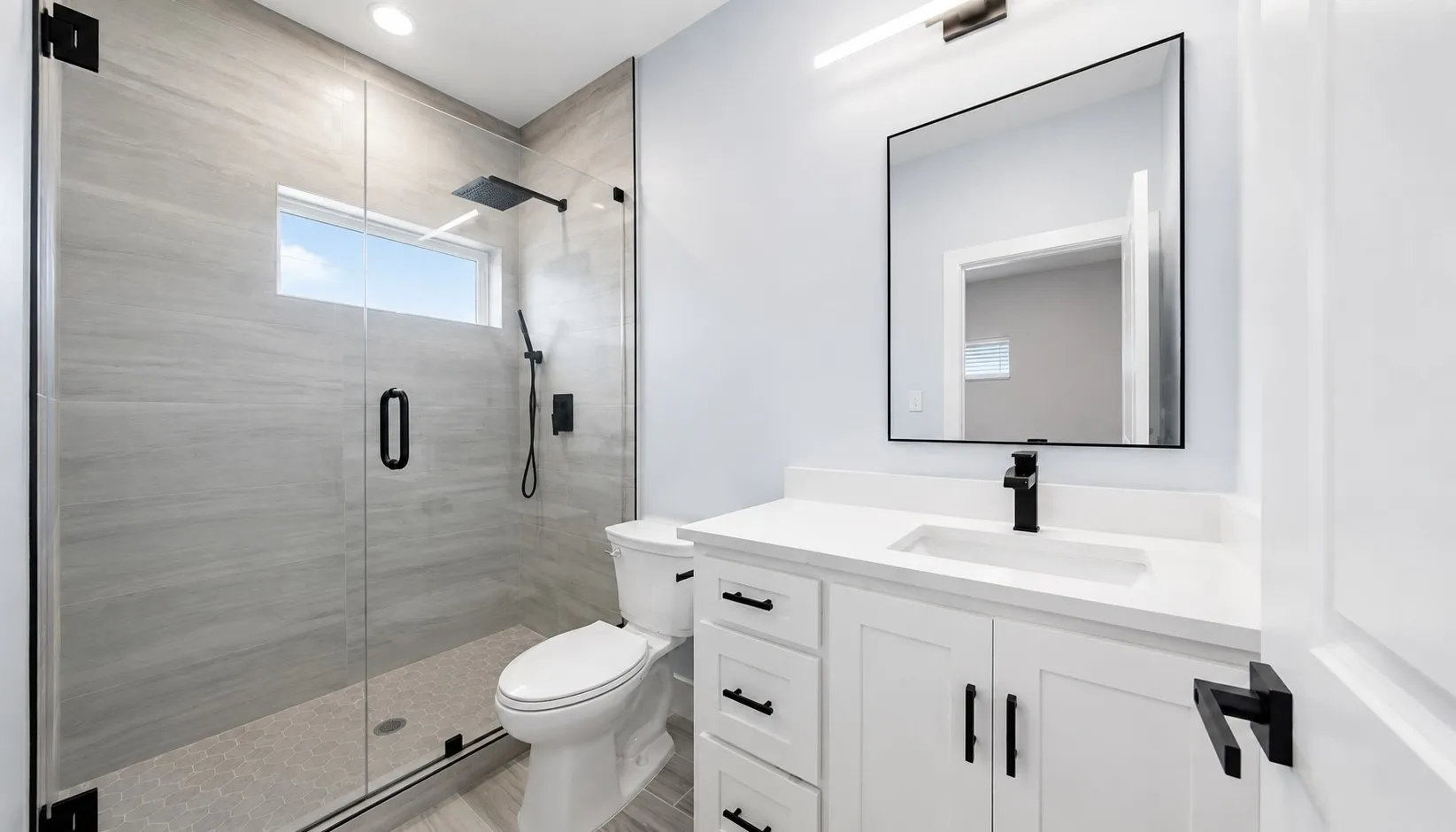 Glass-enclosed shower with matte black fixtures, white vanity with quartz countertop, rectangular undermount sink, and recessed lighting
