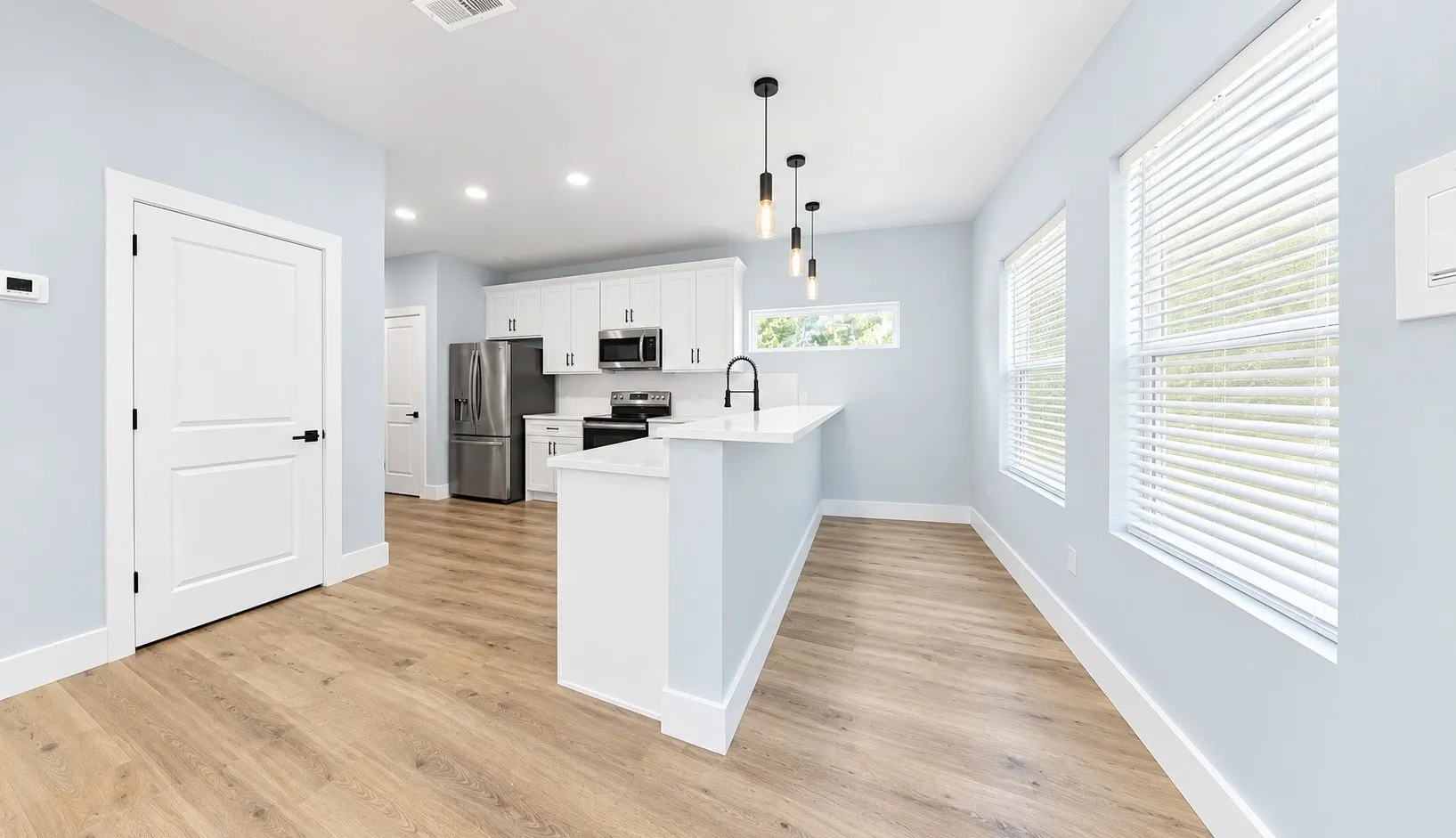 Open-concept kitchen featuring white cabinetry, stainless steel appliances, a white countertop, and wood-finish flooring