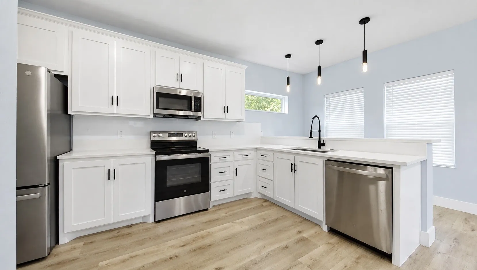 Modern kitchen featuring white shaker cabinetry, stainless steel appliances, light-toned wood-finish flooring, white countertops, and contemporary pendant lighting