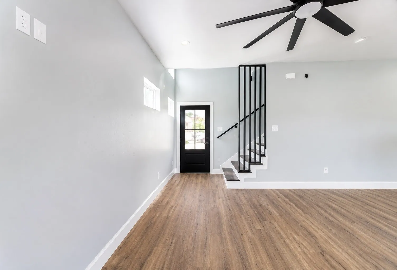 Wood-finish flooring, staircase with contemporary black metal railing, black ceiling fan, black multi-pane door, and recessed lighting