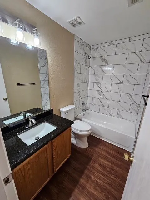 Full bathroom with a textured wall, wood finished floors, vanity, and  shower combination