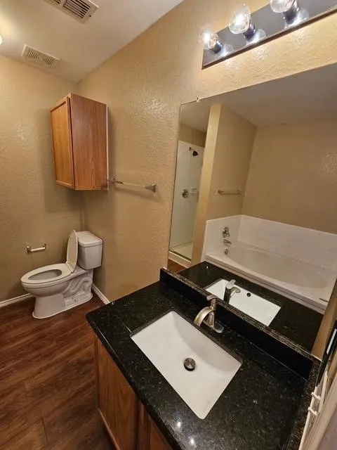 Bathroom featuring a textured wall, a garden tub, vanity, and wood finished floors