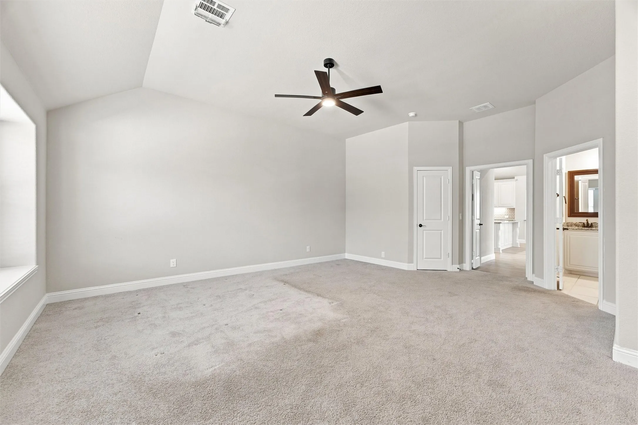 Spacious primary suite featuring neutral carpet flooring, ceiling fan with integrated lighting, and multiple glass-panel doors providing natural light from adjoining spaces