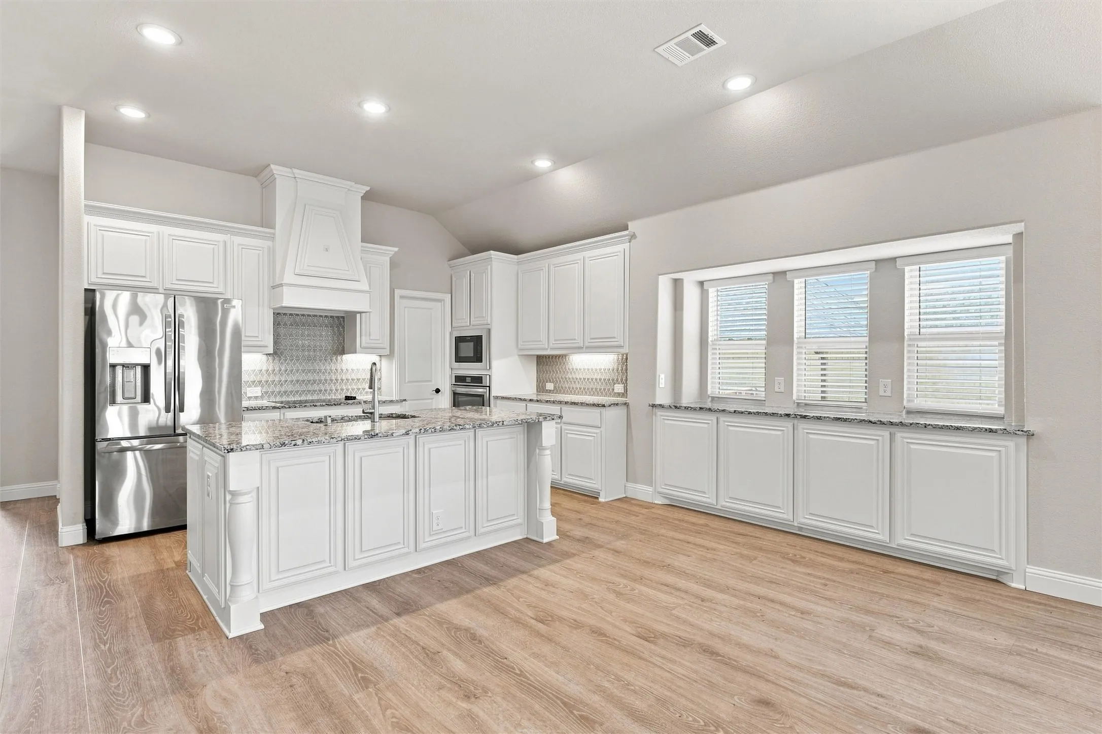 Gourmet kitchen with white cabinetry, granite countertops, stainless steel appliances, and wood-finish flooring