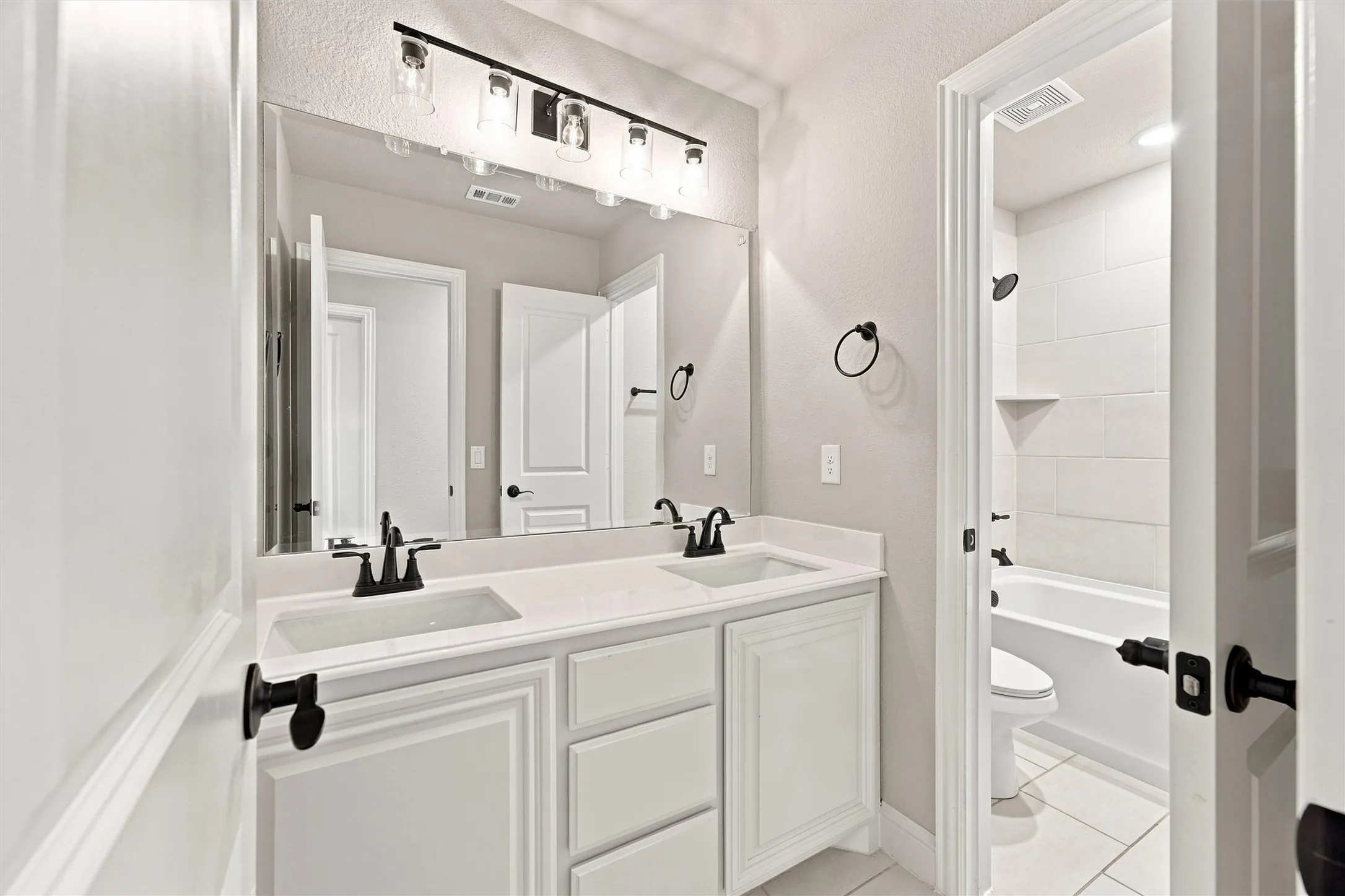 Dual vanity with integrated sinks, white cabinetry, matte black fixtures, and a combined shower/tub with white subway tile surround