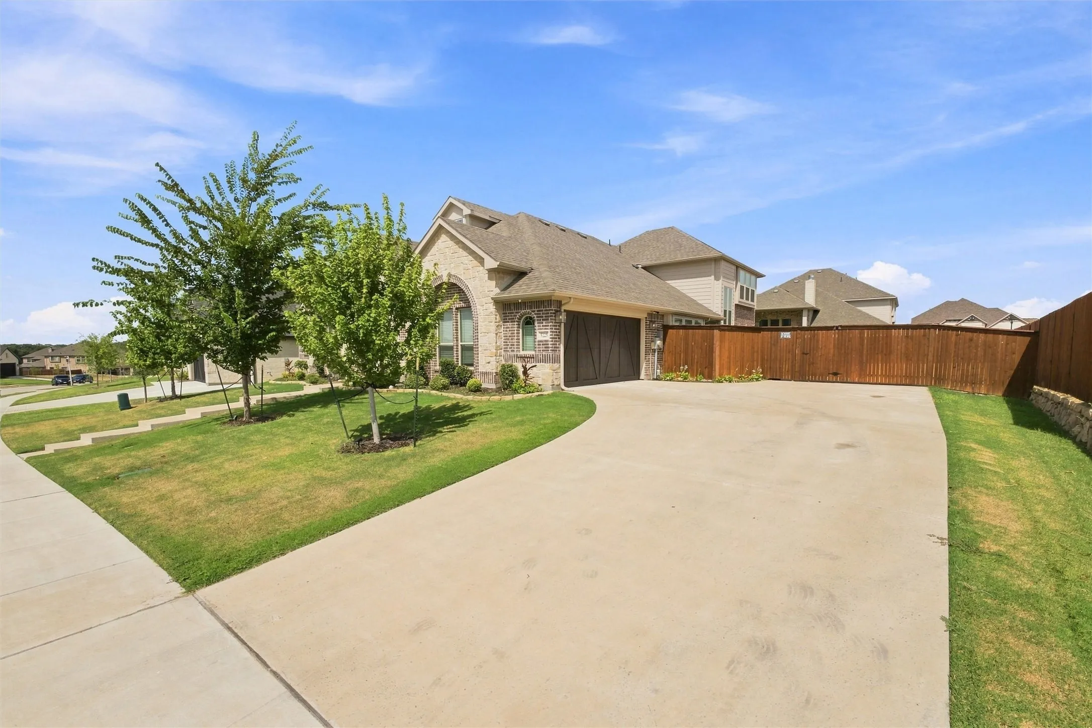 Brick and stone exterior with arched window, concrete driveway, attached garage with wood-finish door, and privacy fencing
