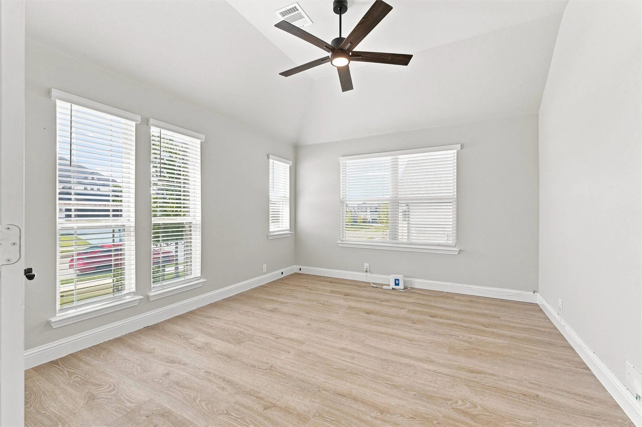 Vaulted ceiling with a contemporary ceiling fan, multiple windows with blinds, and wood-finish flooring