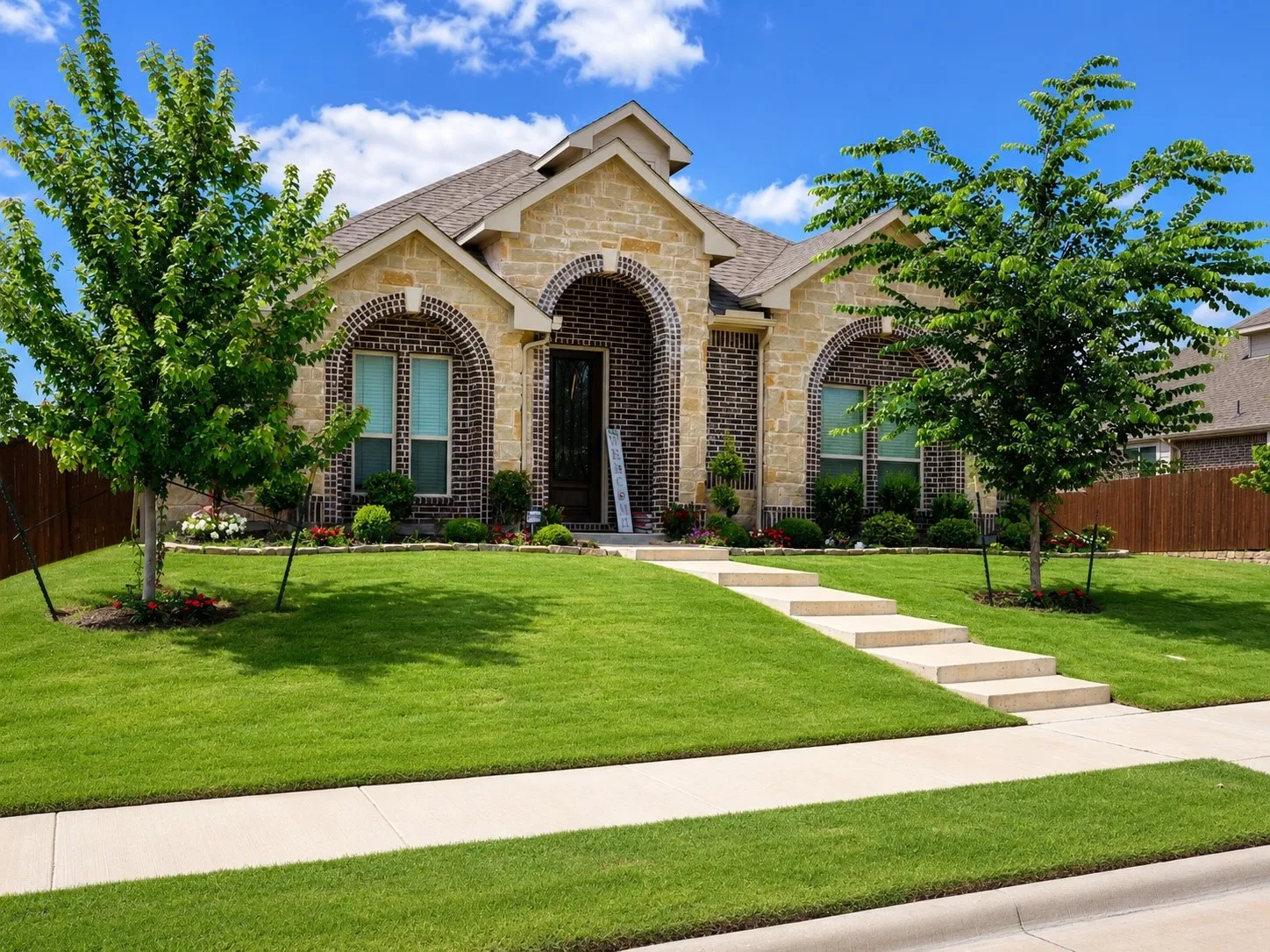 Stone and brick exterior with arched entryway, concrete walkway, and established landscaping