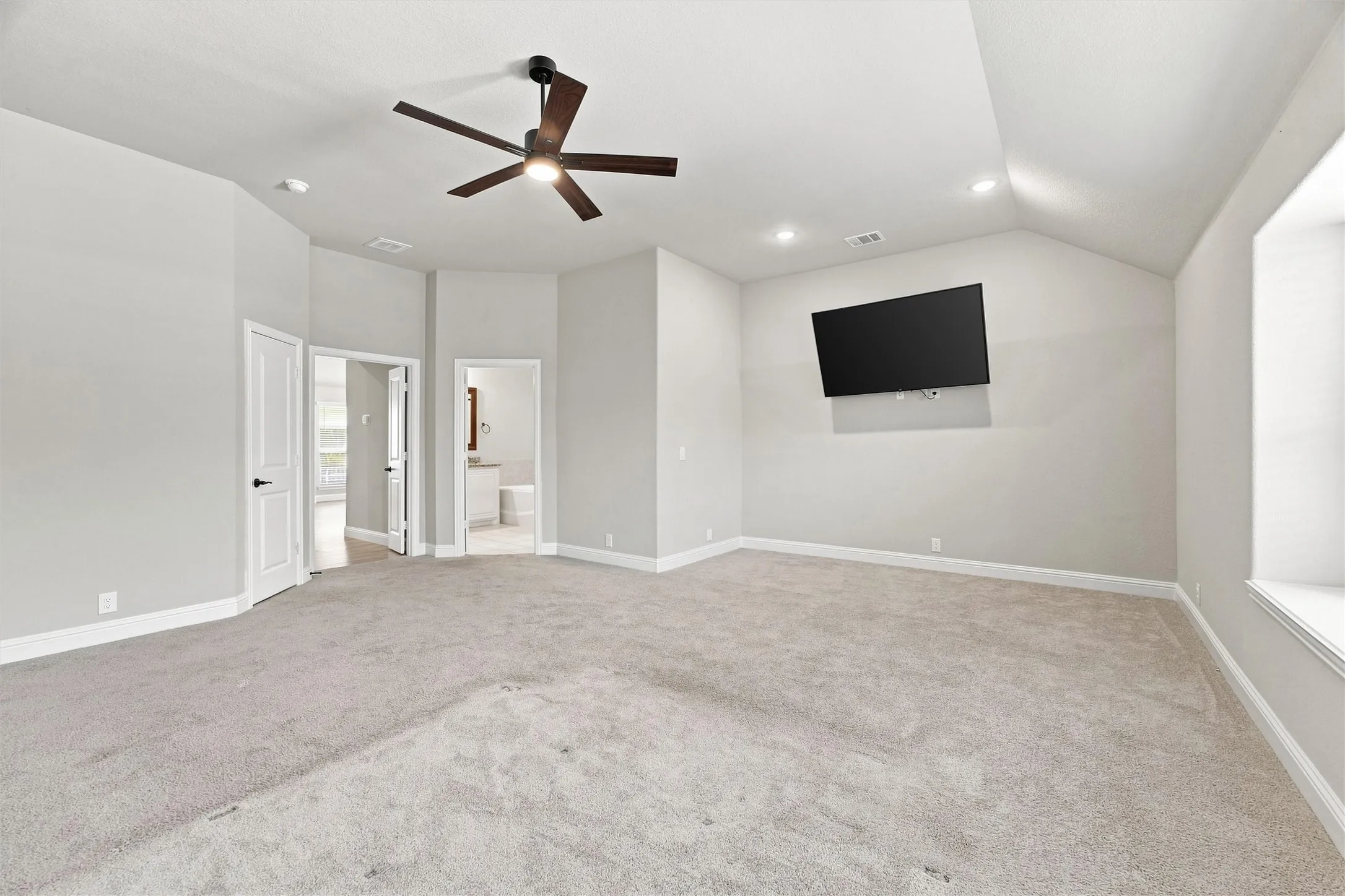 Spacious room featuring vaulted ceilings, recessed lighting, a modern ceiling fan, and light gray carpeting