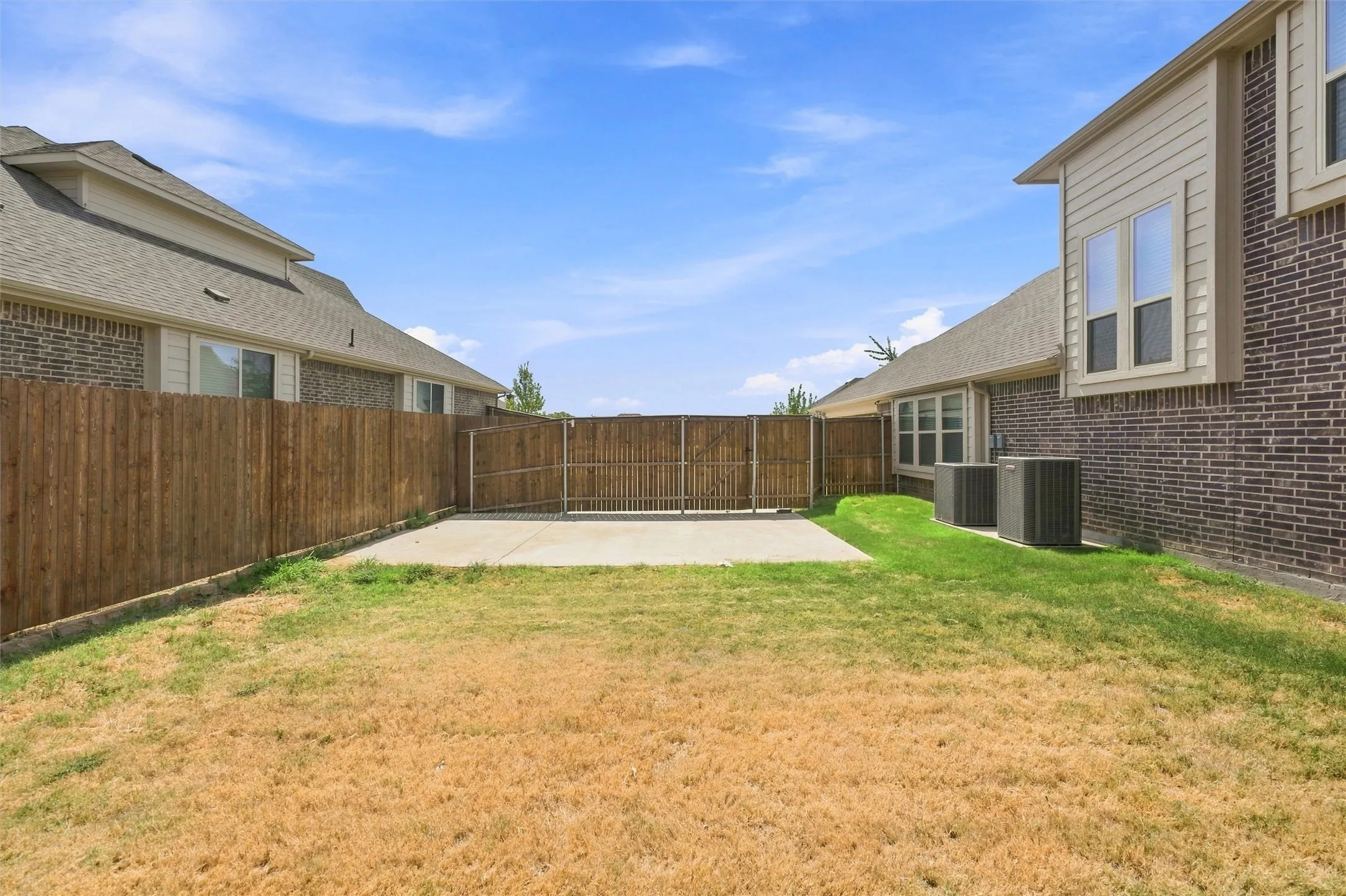 Spacious backyard featuring a freshly poured concrete patio, mature landscaping with established lawn areas, and sturdy wood-finish privacy fencing
